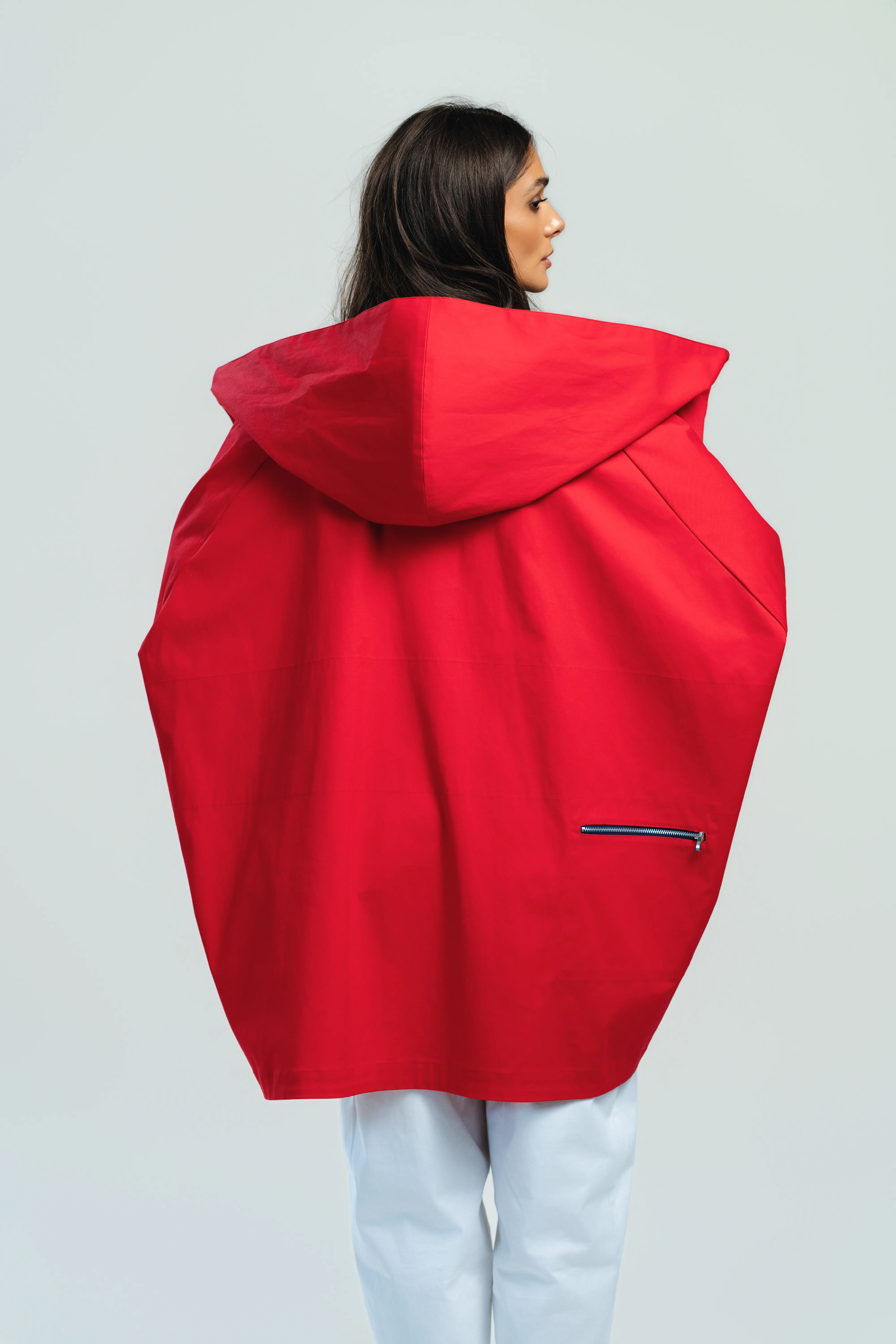 The same red hooded coat seen from behind, its sculptural cocoon-like silhouette filling the frame