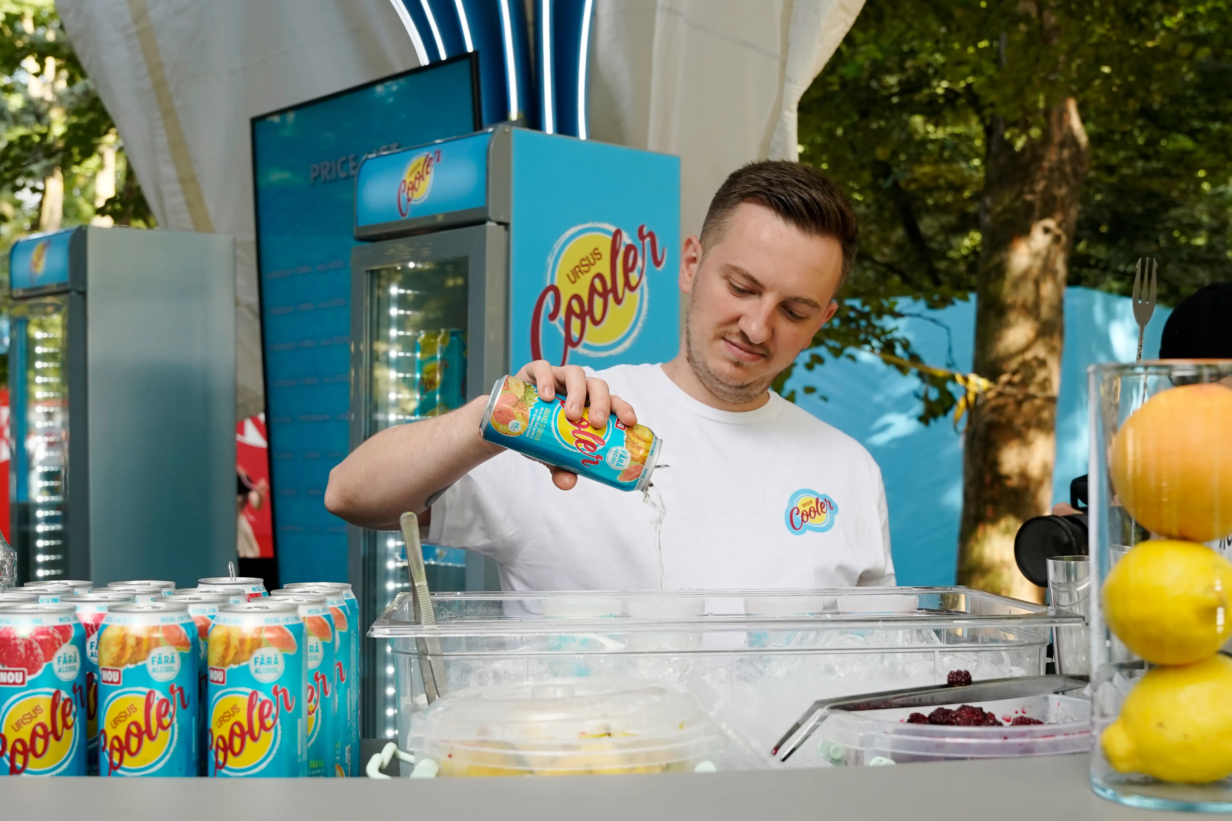 A bartender pours a canned cocktail over ice at a branded festival drinks stand