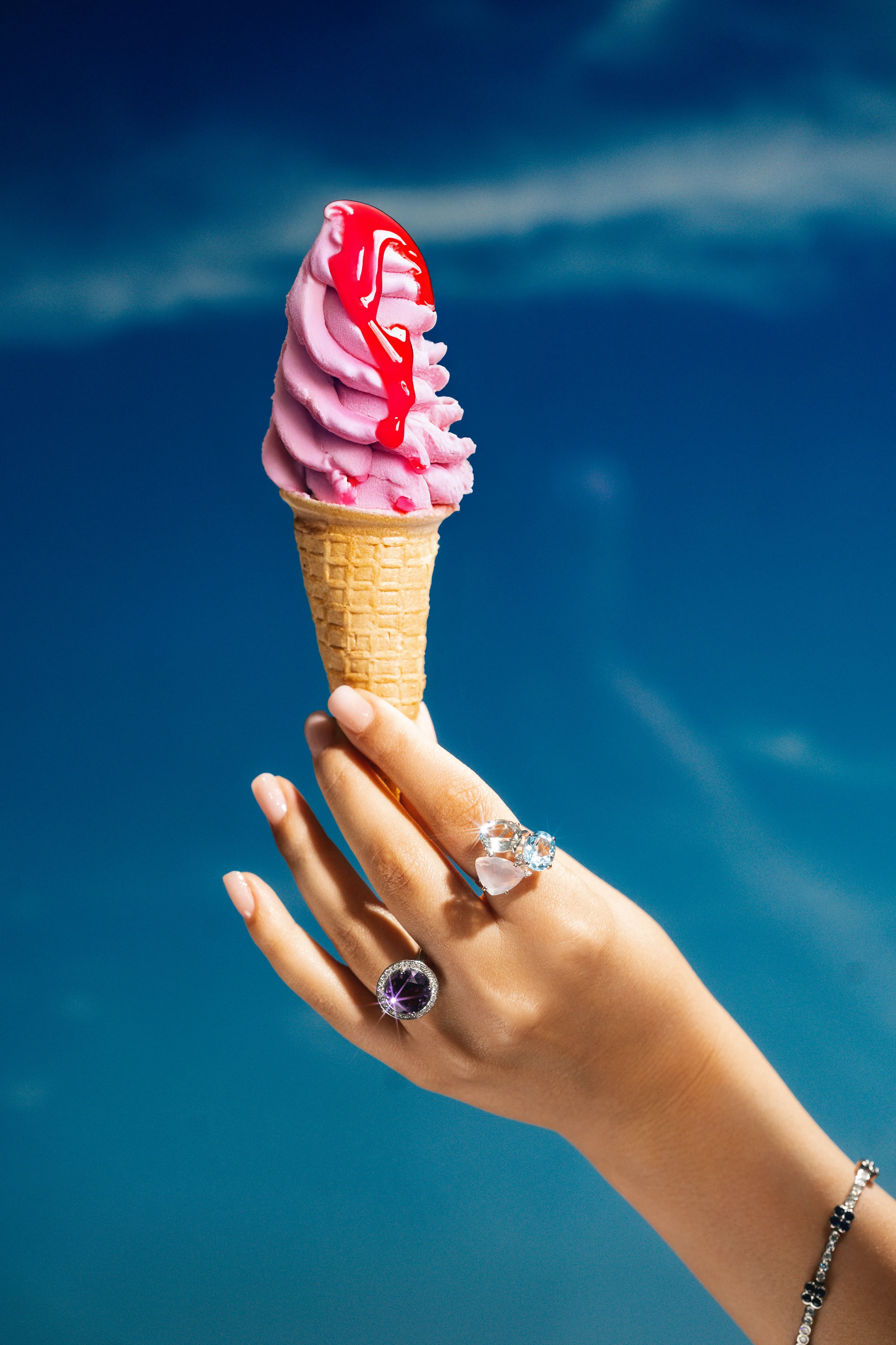 An ice cream cone dripping with pearls against a clear blue sky, a jeweled hand holding the cone