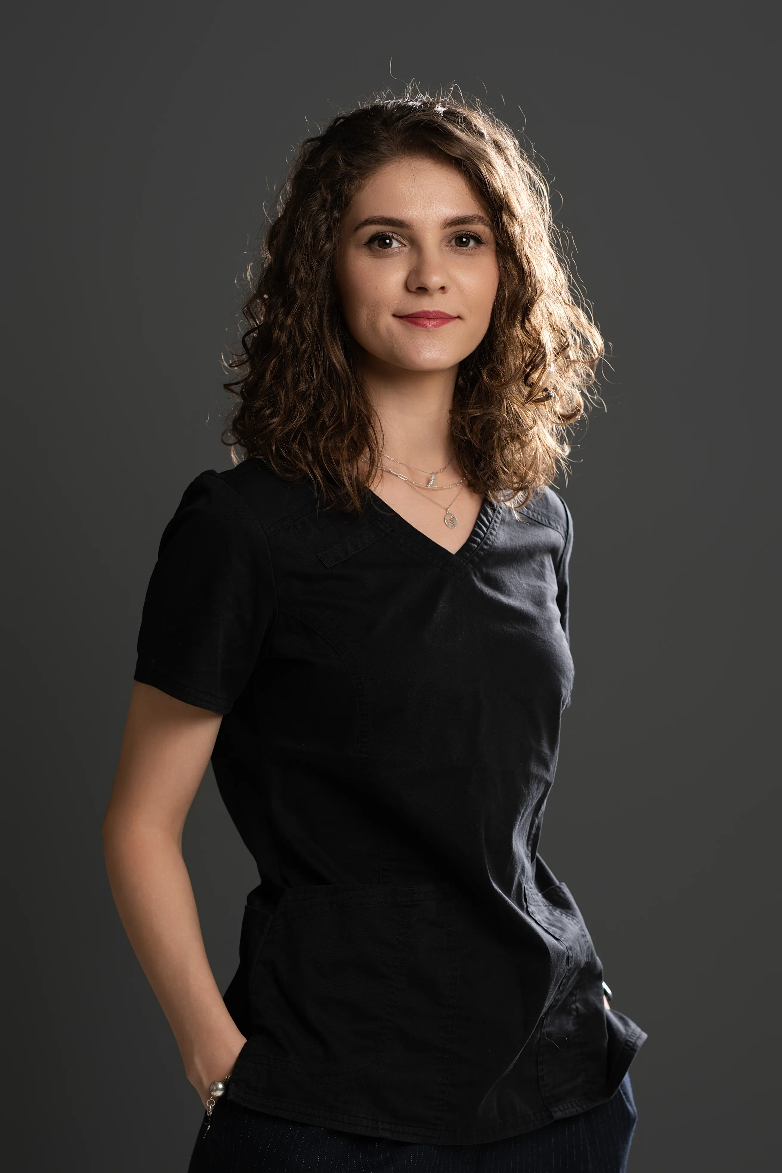 Woman in a black v-neck top, dramatic side-lit studio portrait, hand in pocket
