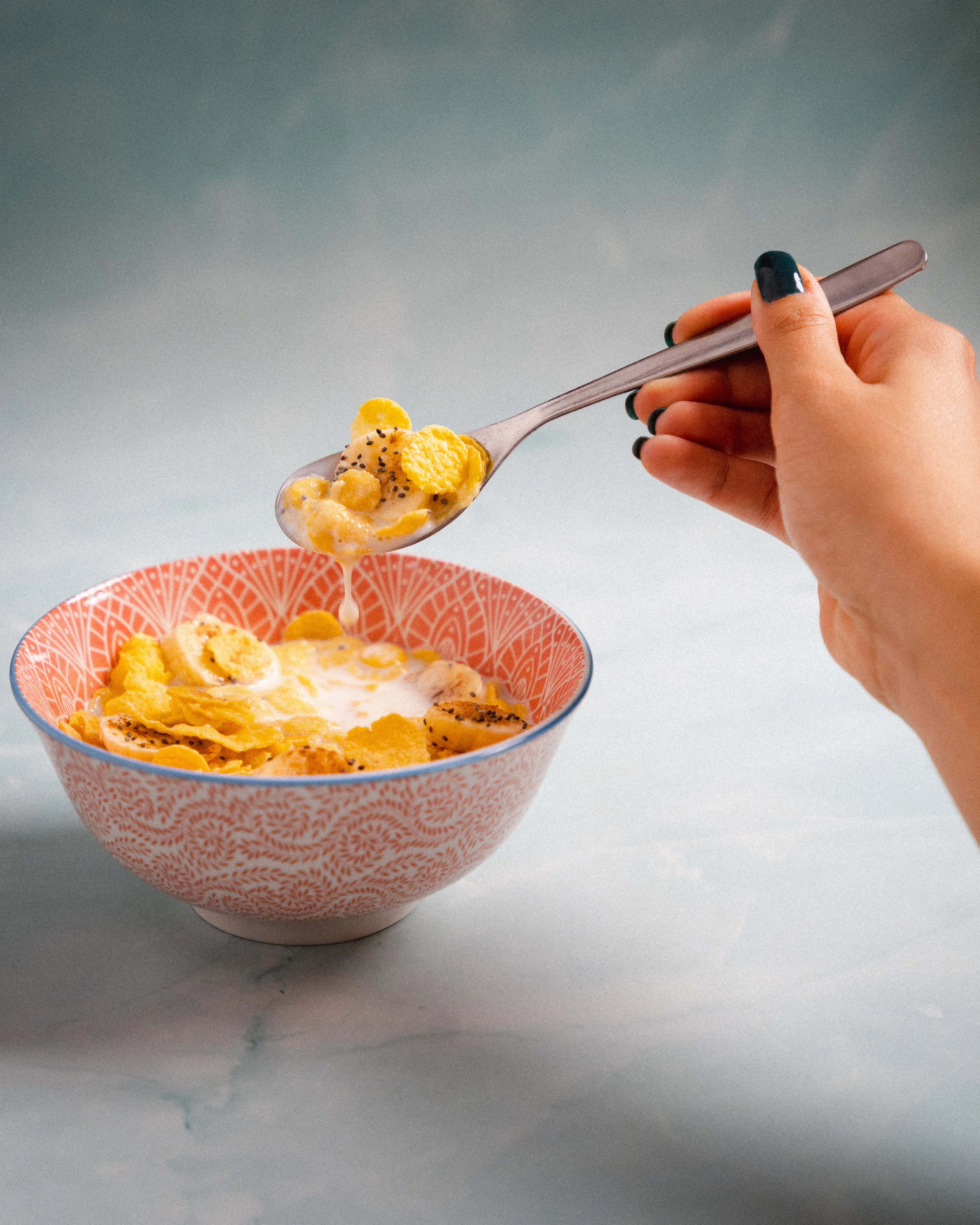 A hand lifting a spoonful of cereal from a pink bowl