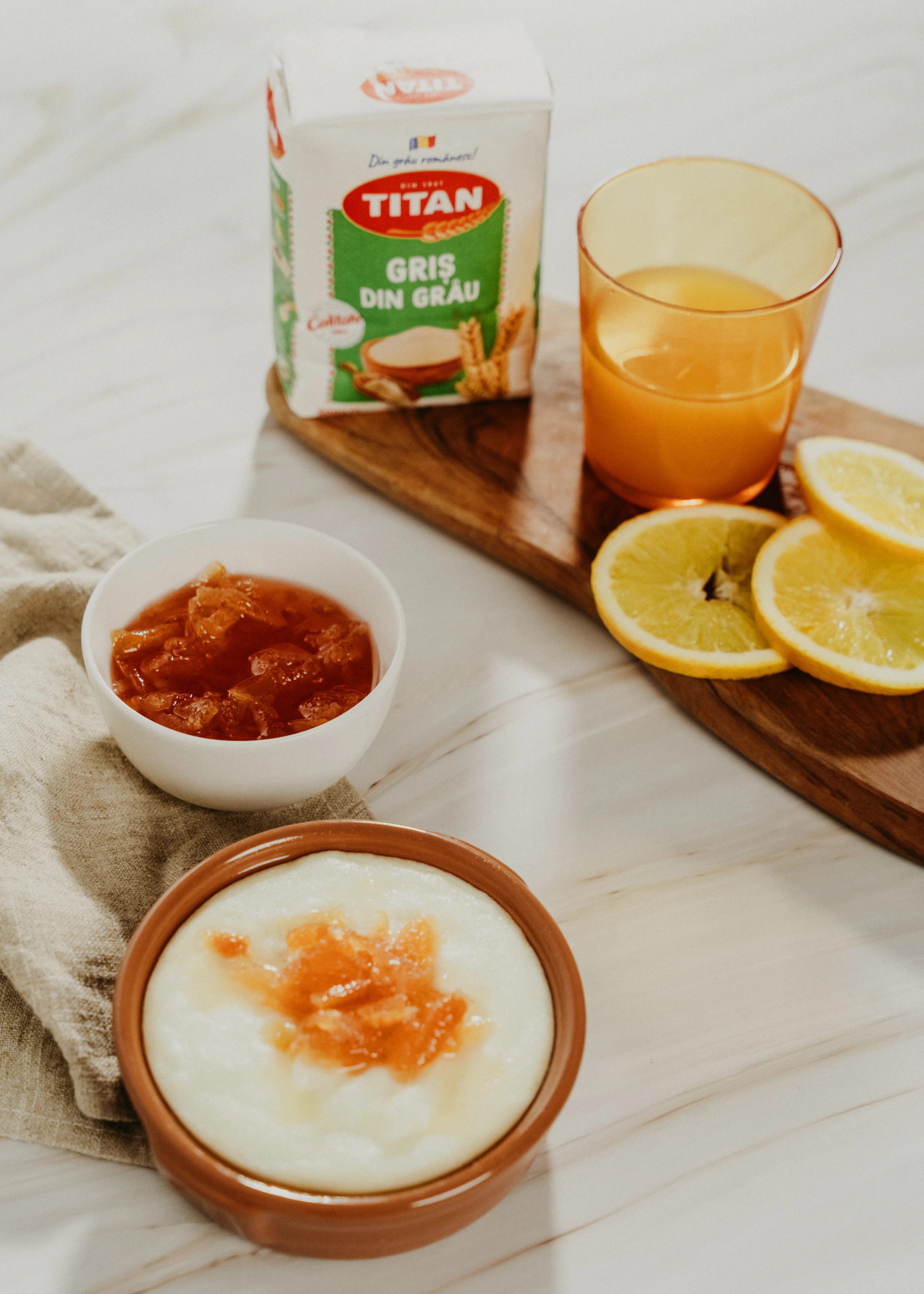 A styled breakfast scene with semolina porridge, jam, orange juice, and sliced citrus