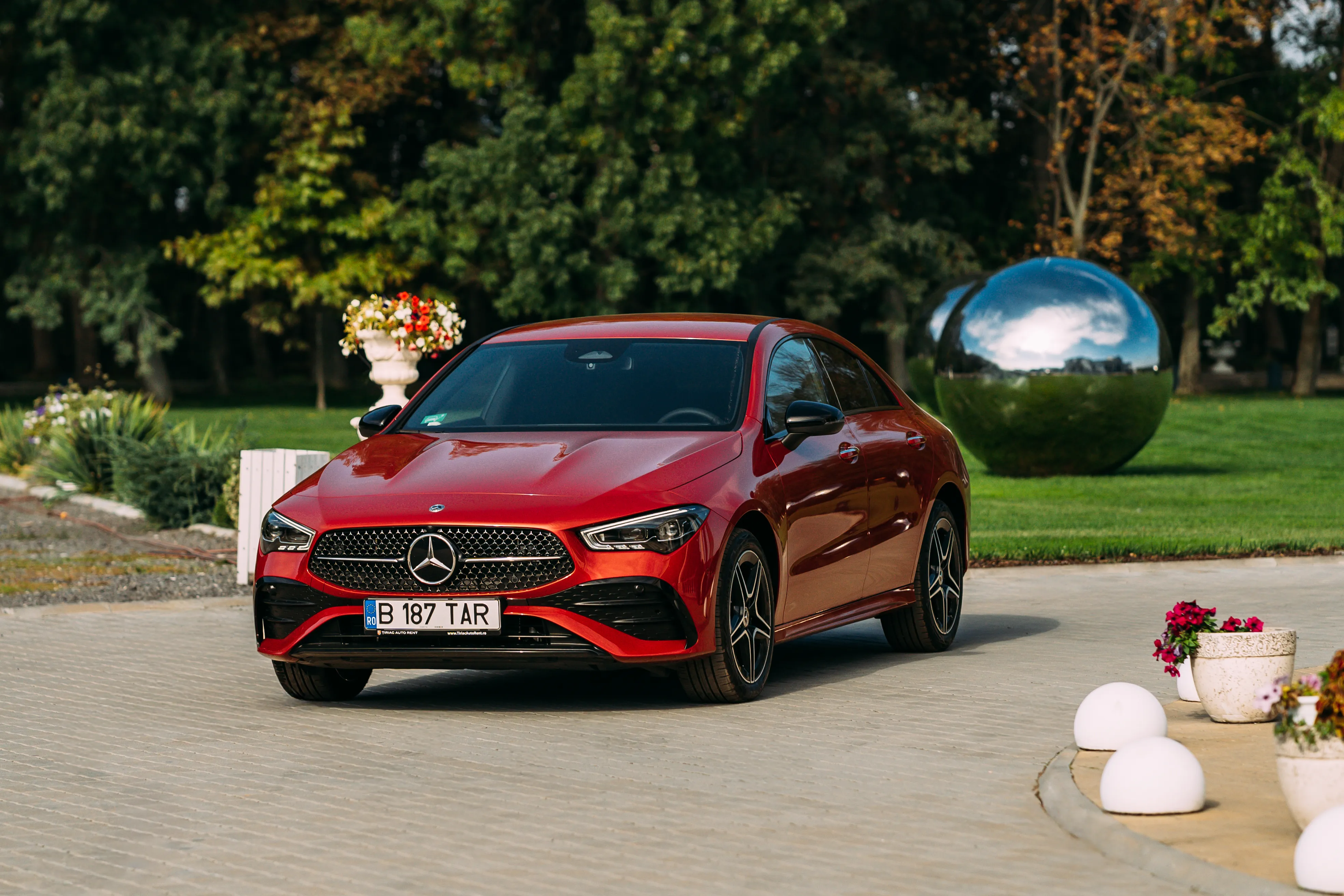 Red Mercedes-Benz CLA in daylight, front three-quarter view in a manicured garden driveway