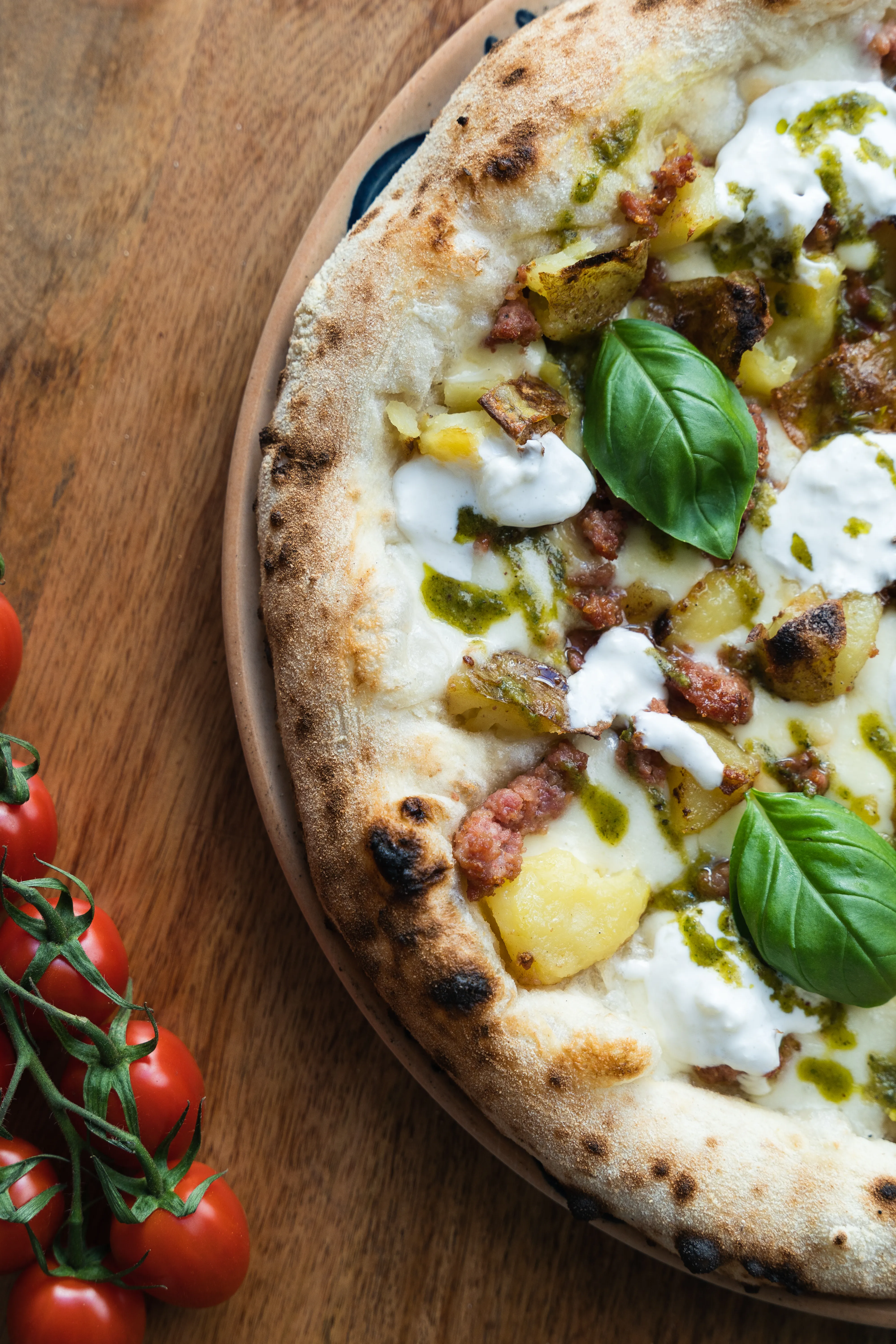 Close-up of a wood-fired pizza with potato, sausage, and burrata