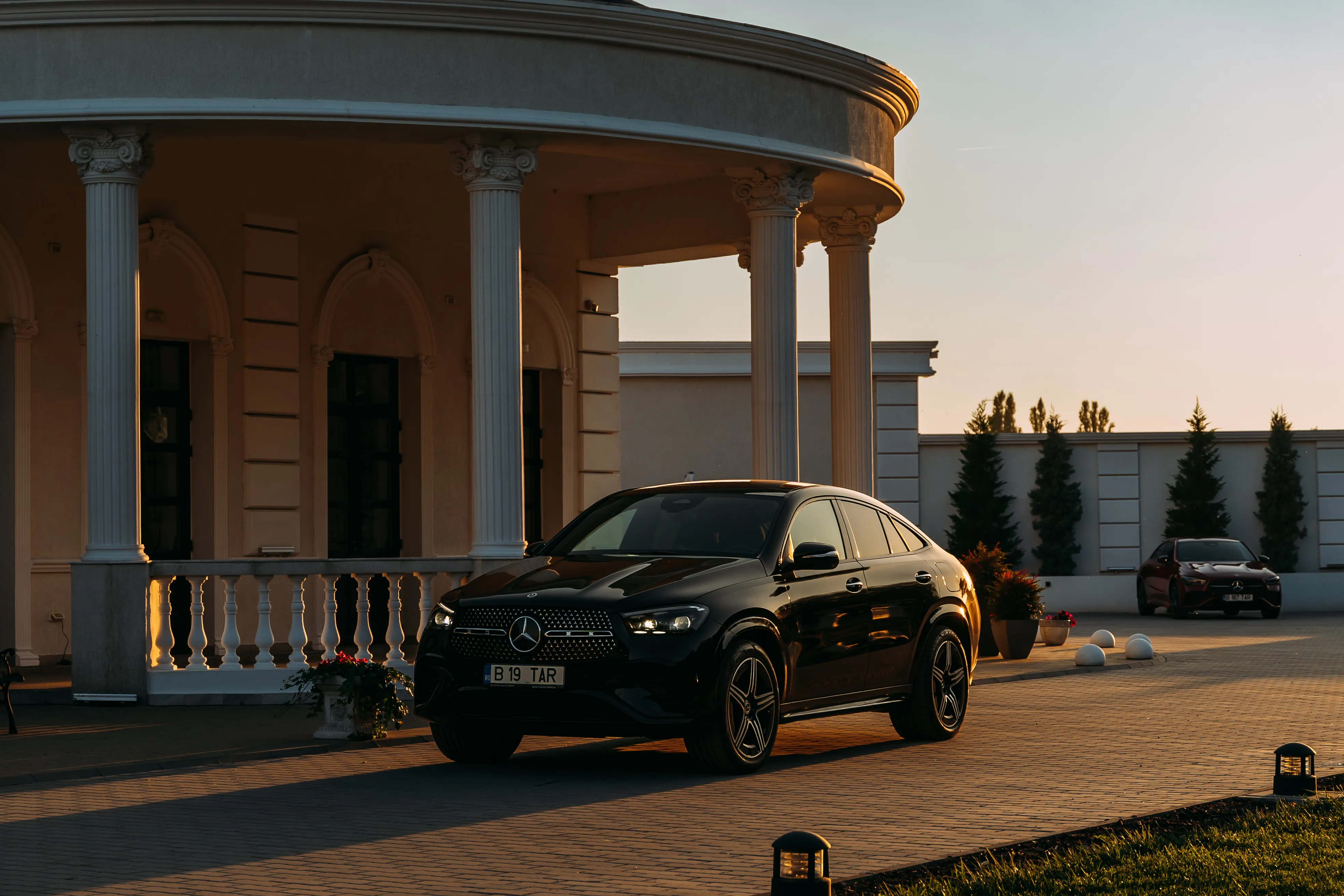 Black Mercedes-Benz GLC Coupe arriving at a colonnaded villa entrance at dusk