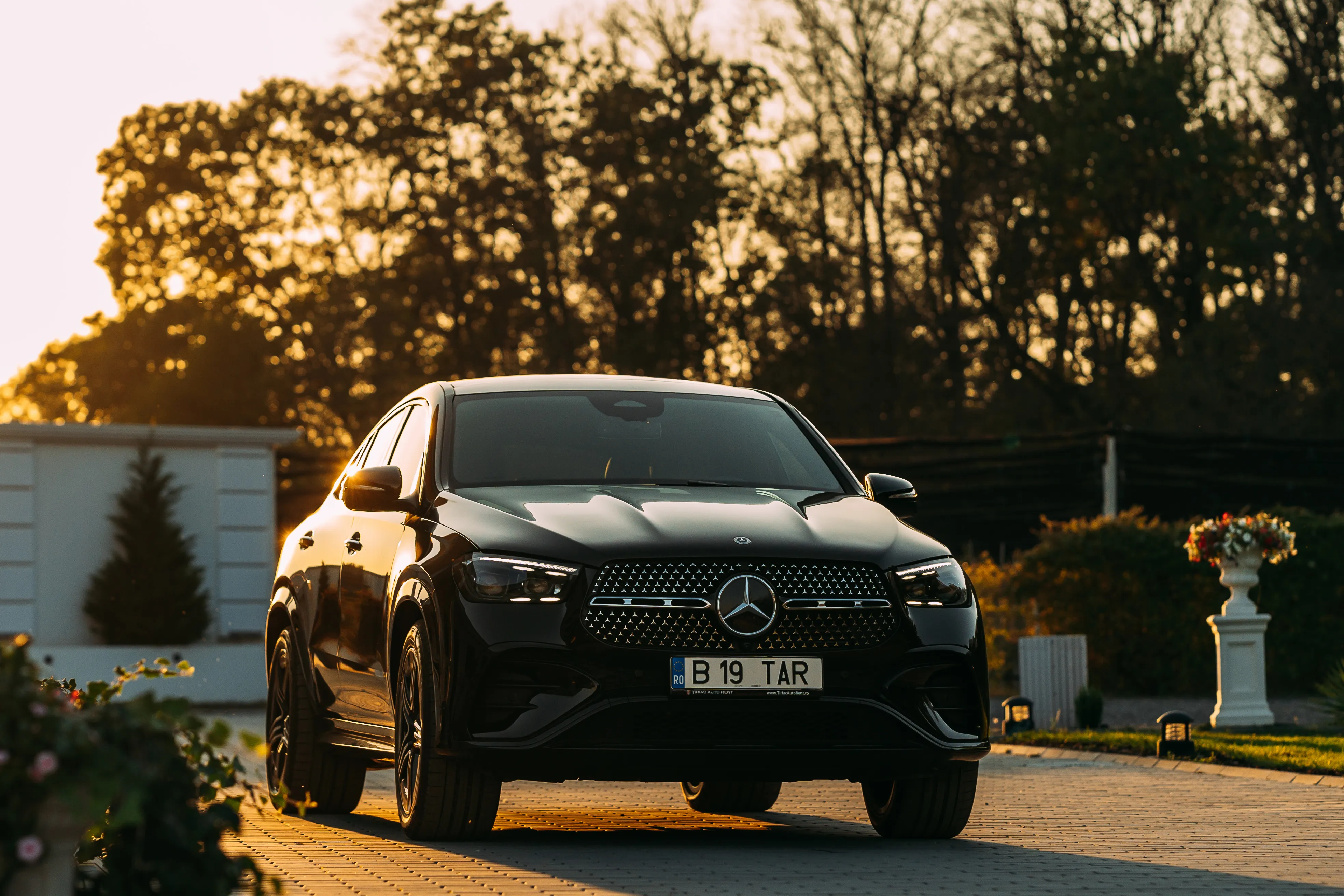 Black Mercedes-Benz GLC Coupe head-on at golden hour, backlit by low sun through trees