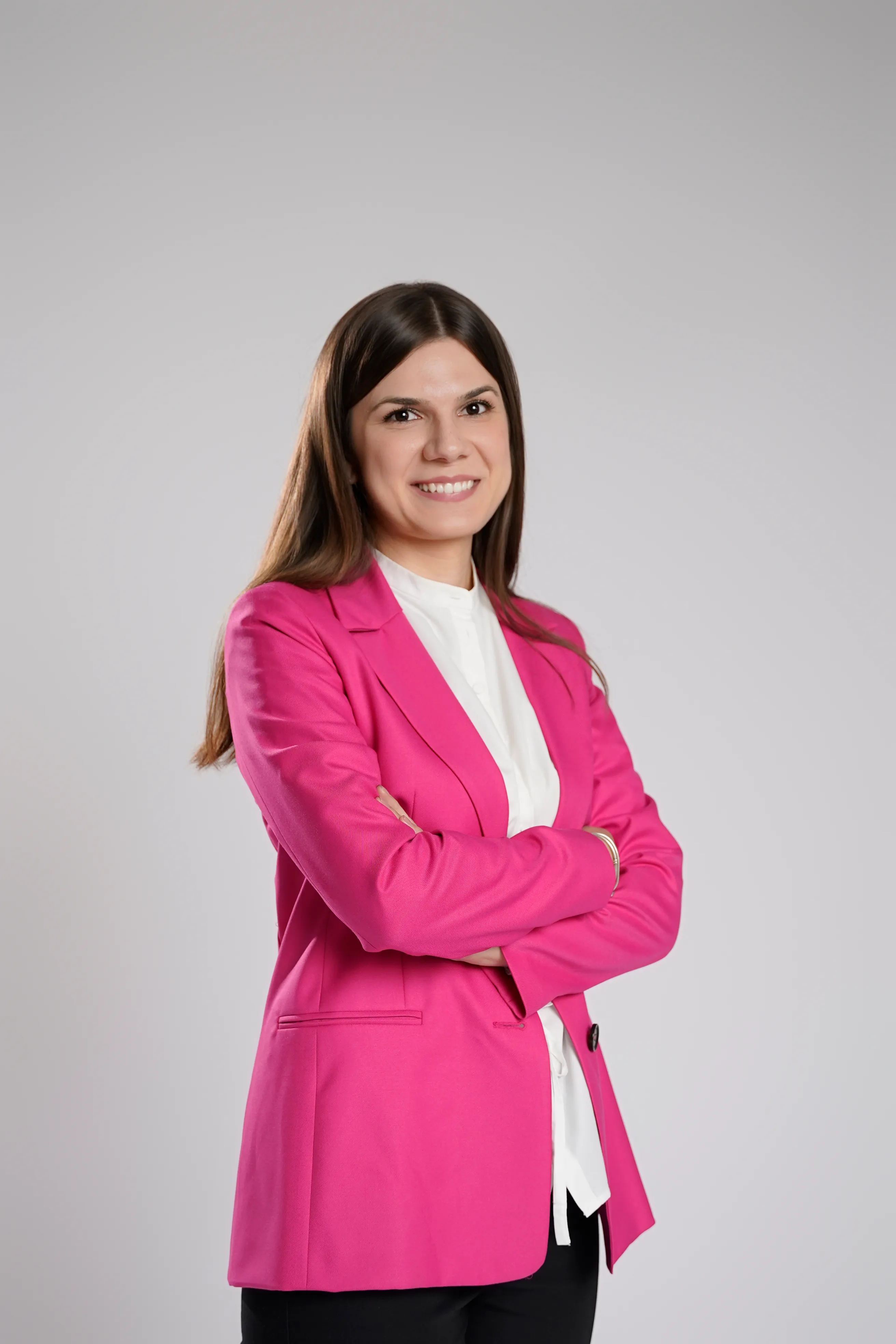 Woman in a magenta blazer, arms crossed, smiling, studio portrait