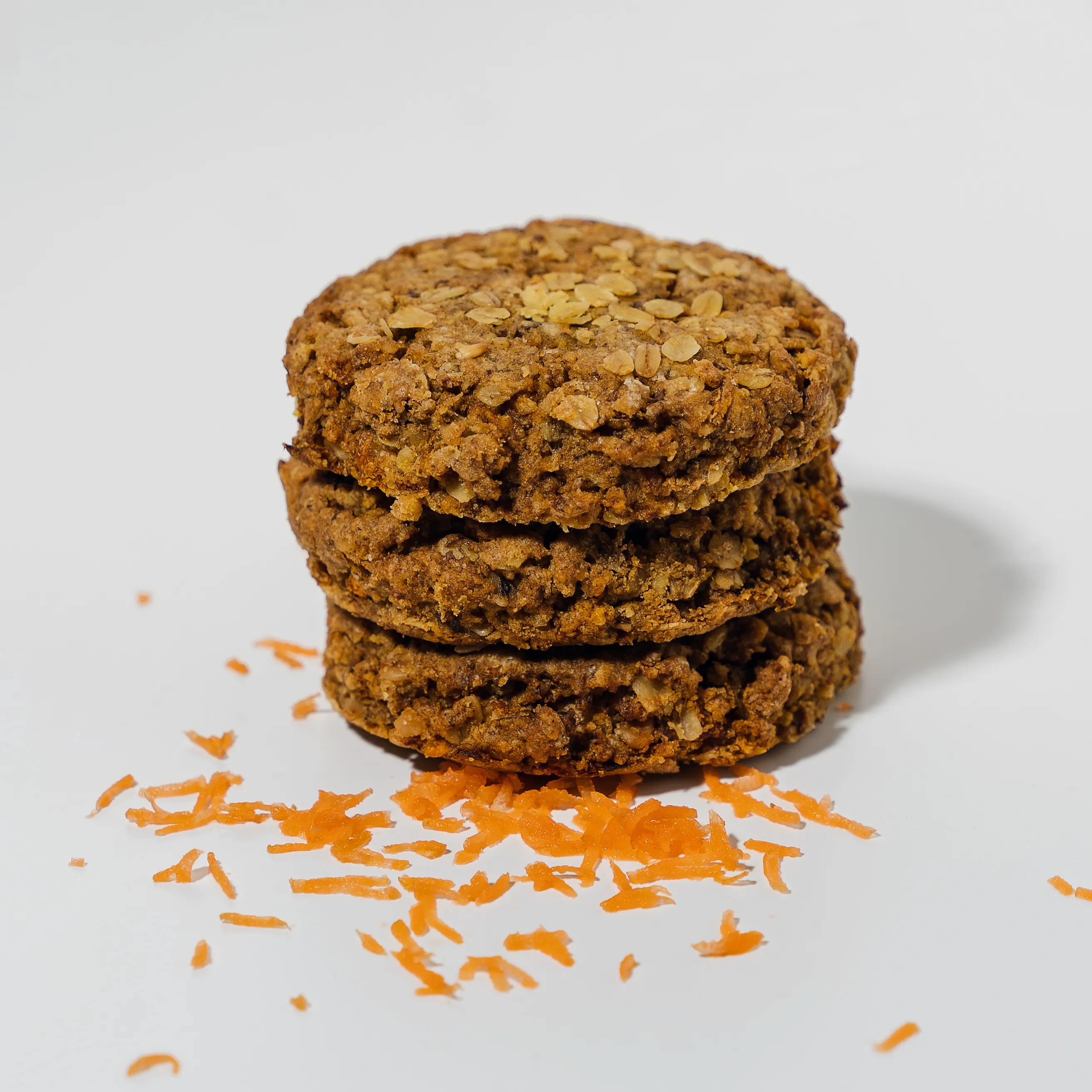 A stack of three oat and carrot cookies with grated carrot scattered beside them