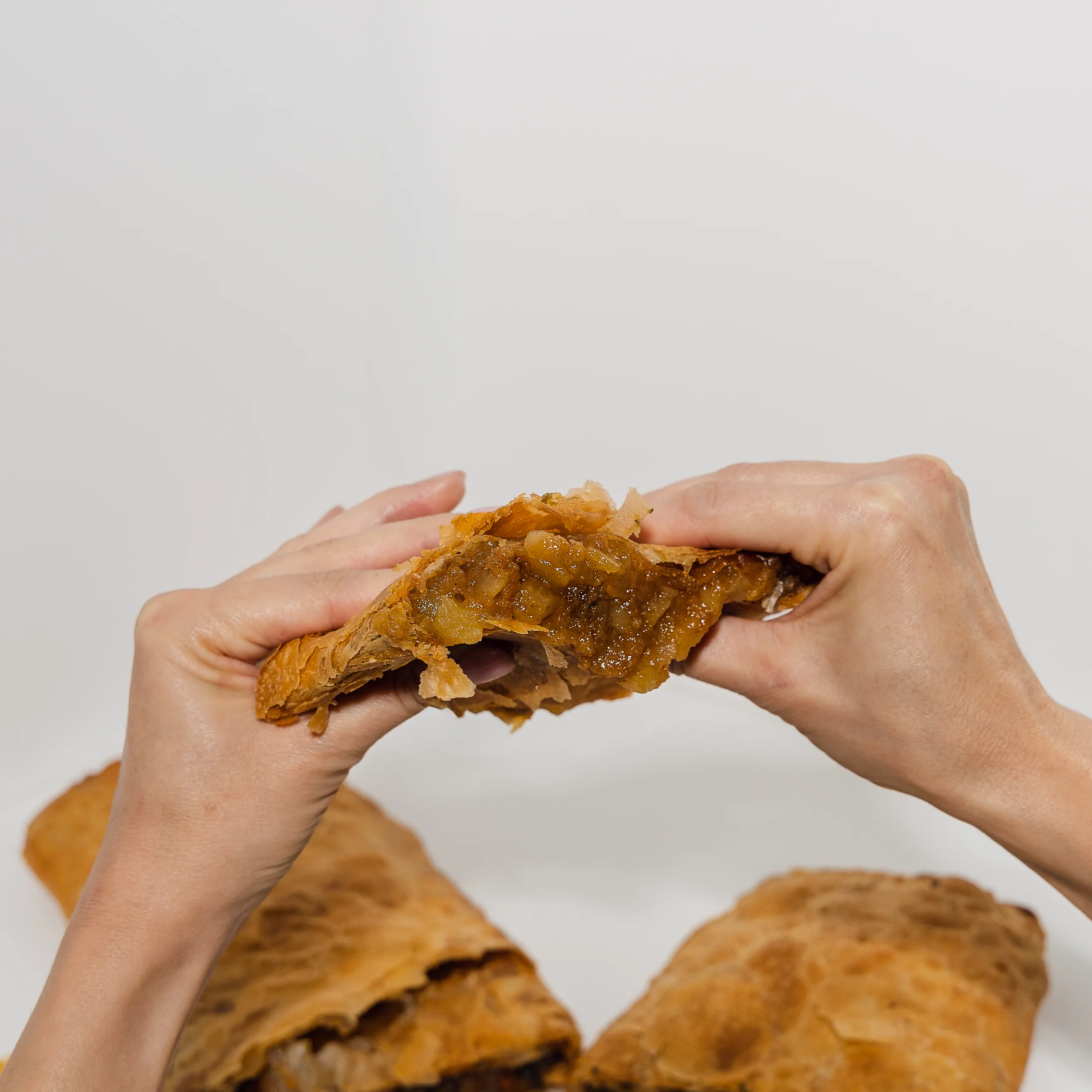 Two hands pulling apart a filled pastry, the warm filling stretching between them