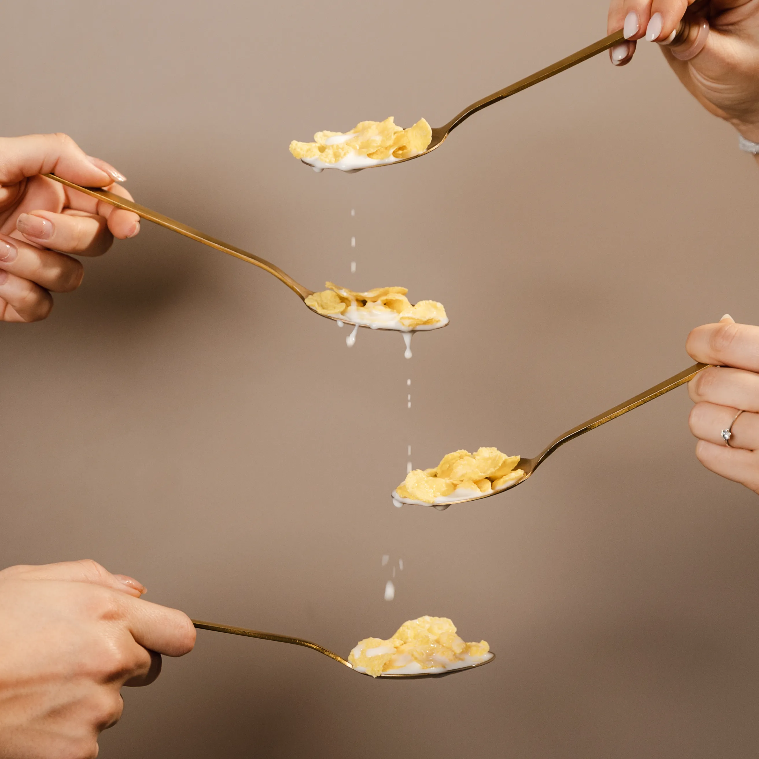 Four spoons pouring cereal and milk in a stop-motion sequence against a warm brown background