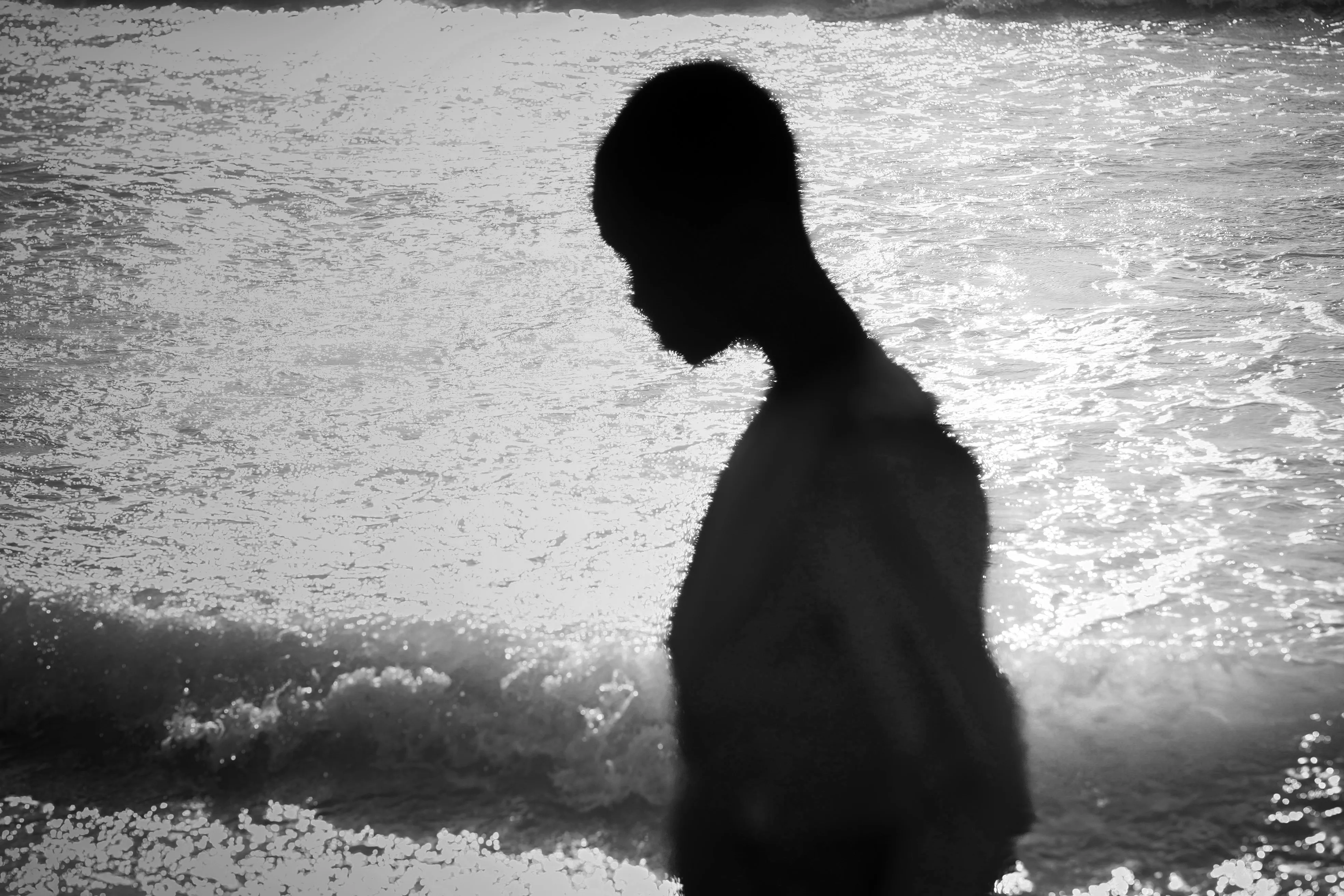 A silhouetted figure stands at the shoreline, backlit by sunlit waves