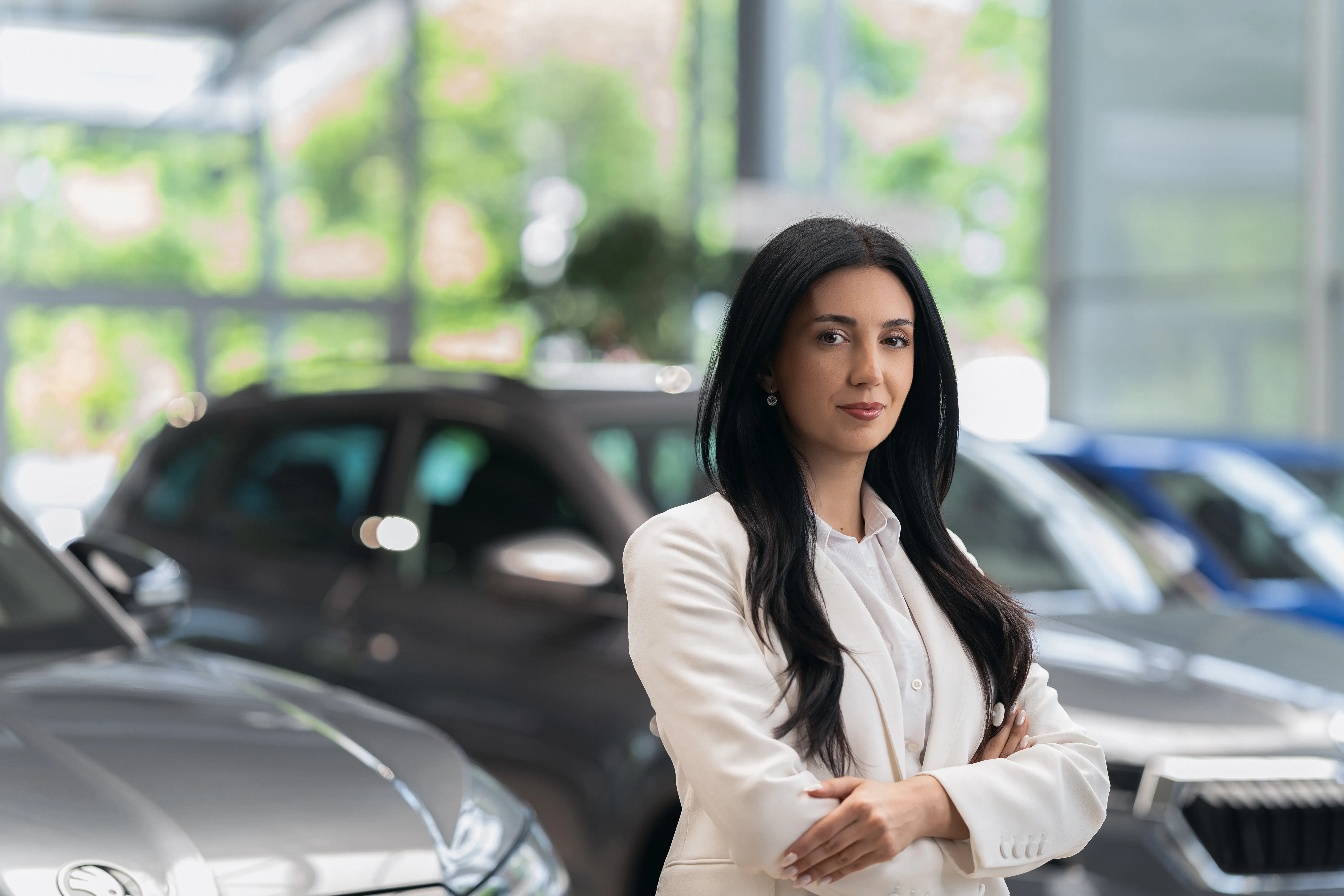 Portrait of a Brady Auto Center advisor in a white blazer, arms crossed, showroom cars behind her