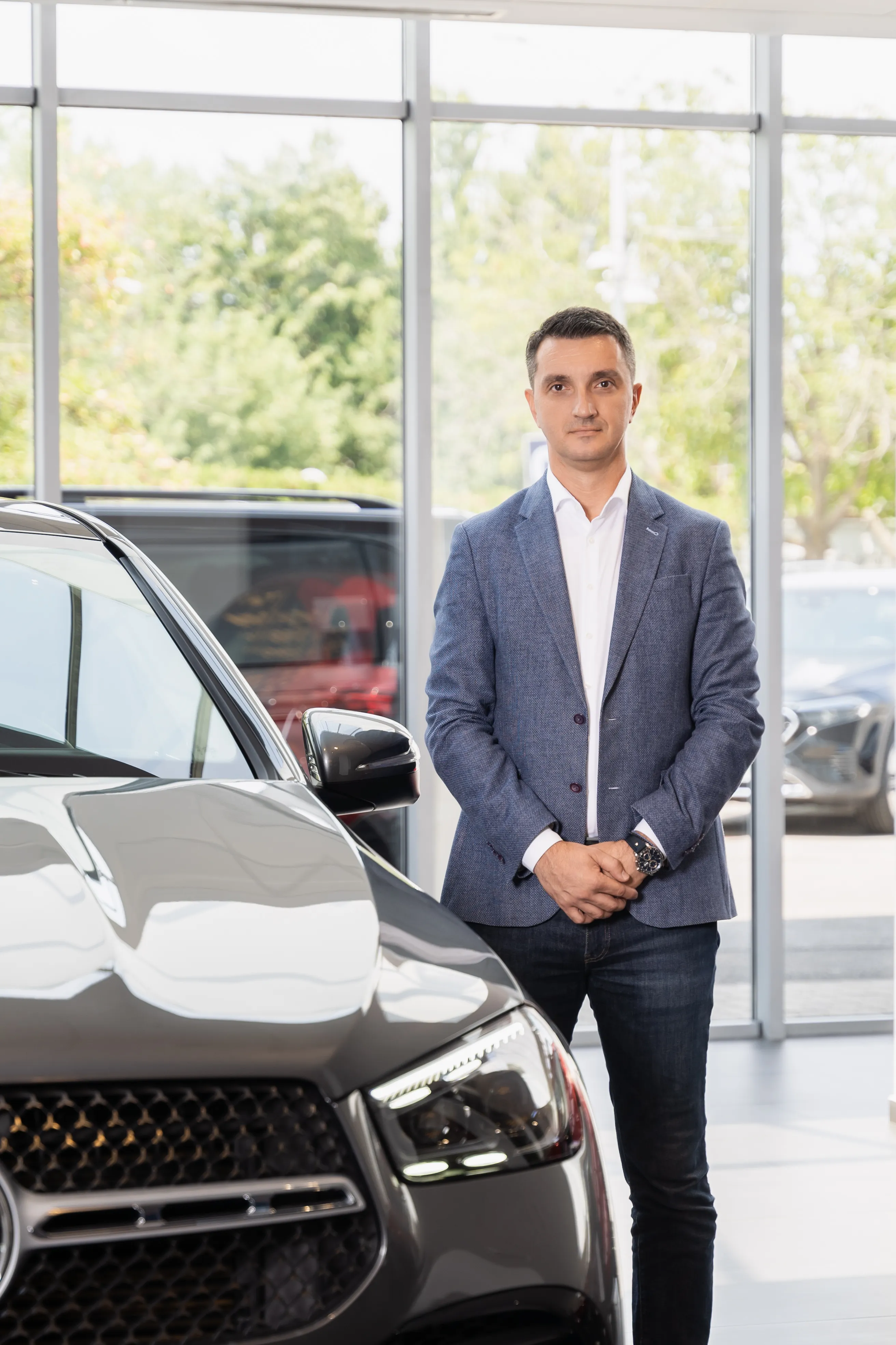 Man in a blazer standing beside a car in a dealership showroom