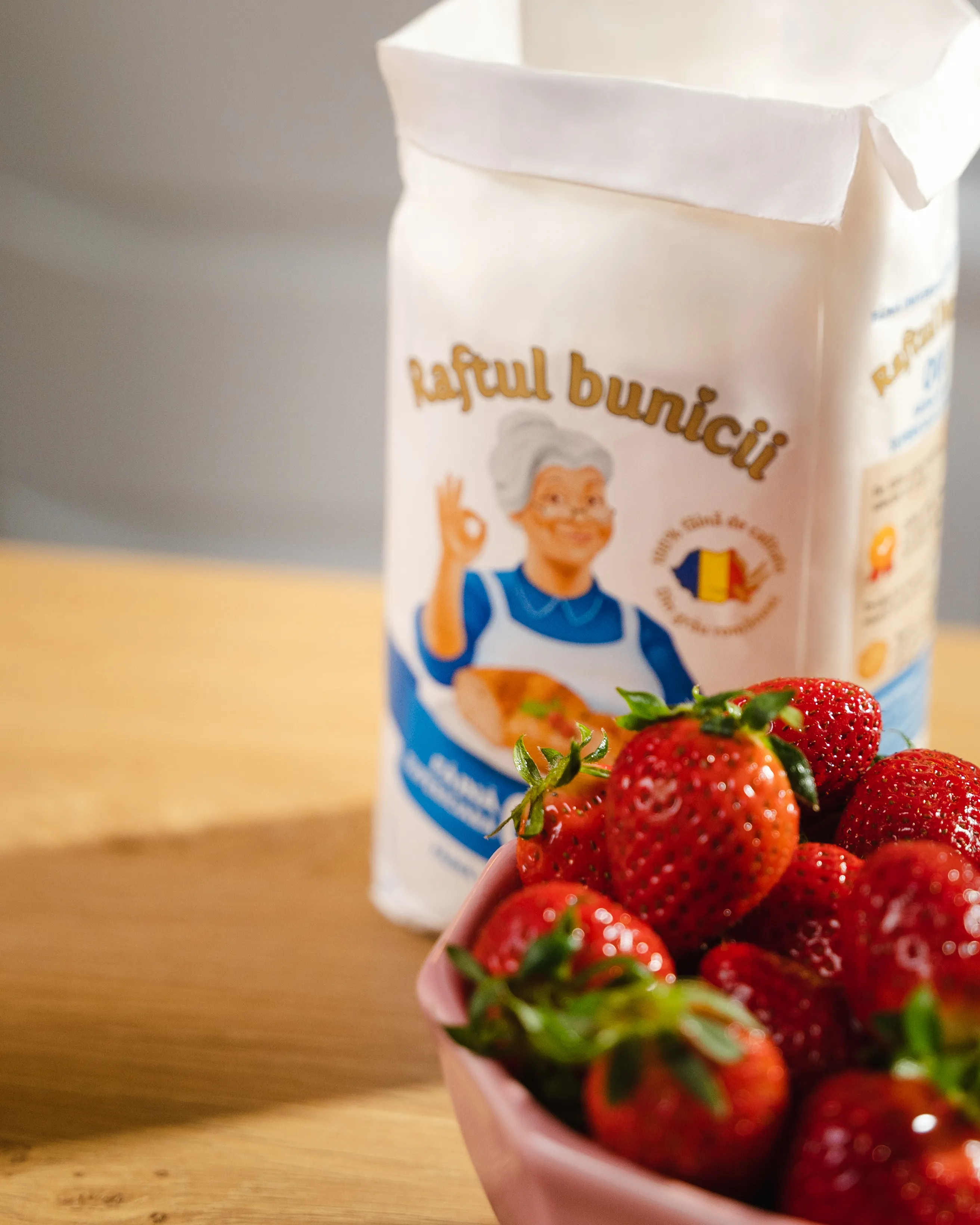 Fresh strawberries in a bowl beside a bag of Raftul Bunicii flour