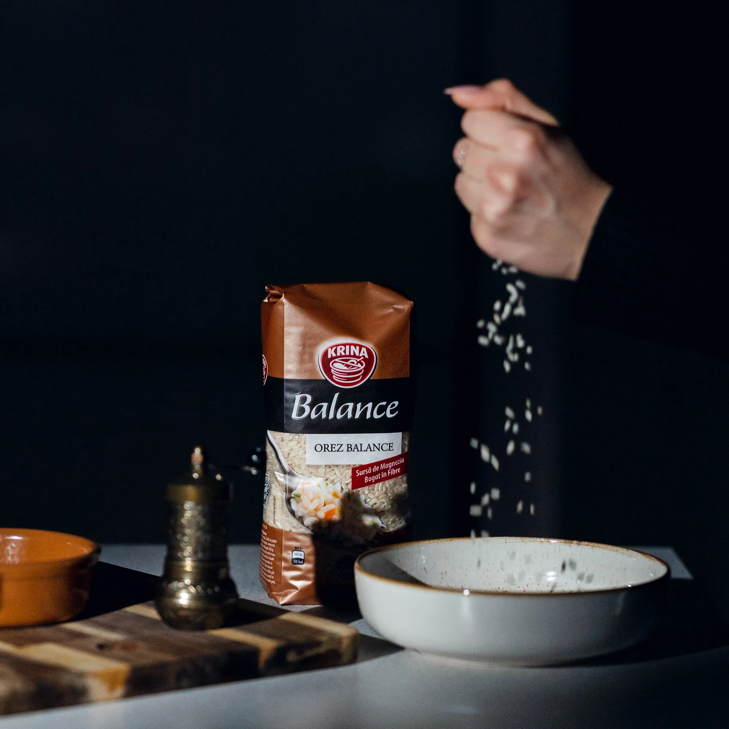 A hand sprinkling seasoning over bowls, lit dramatically against a dark background