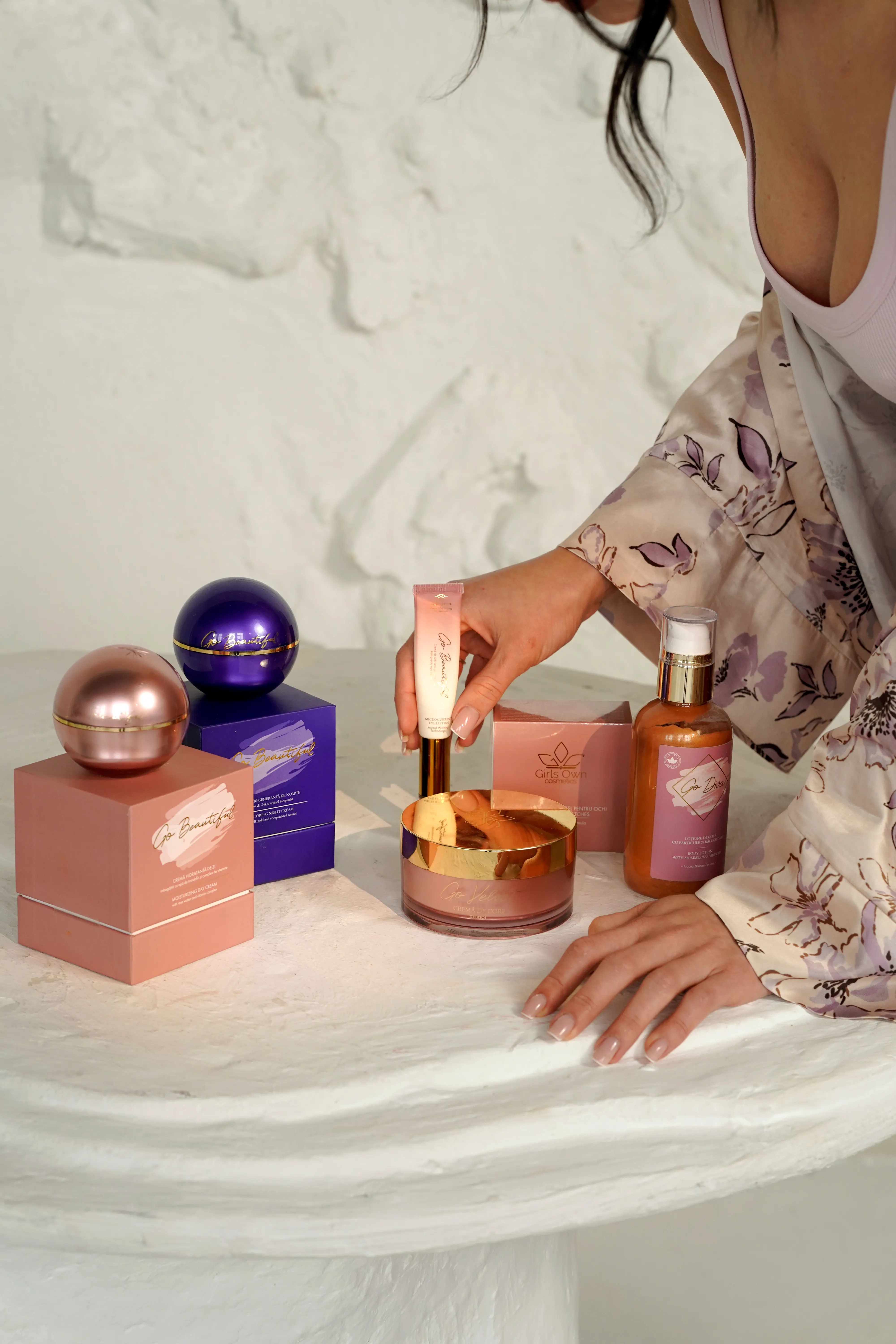 Luxury cosmetics flatlay with spherical jars and boxes against a warm stone backdrop, a hand applying eye cream
