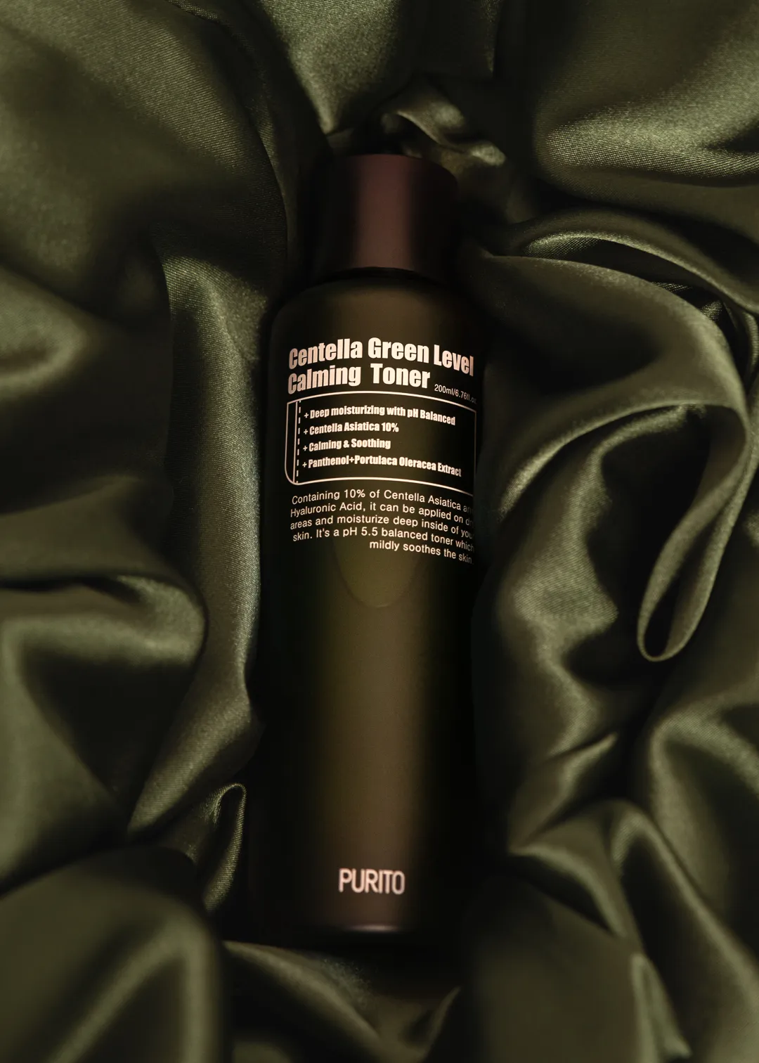 A skincare toner bottle on dark green satin fabric