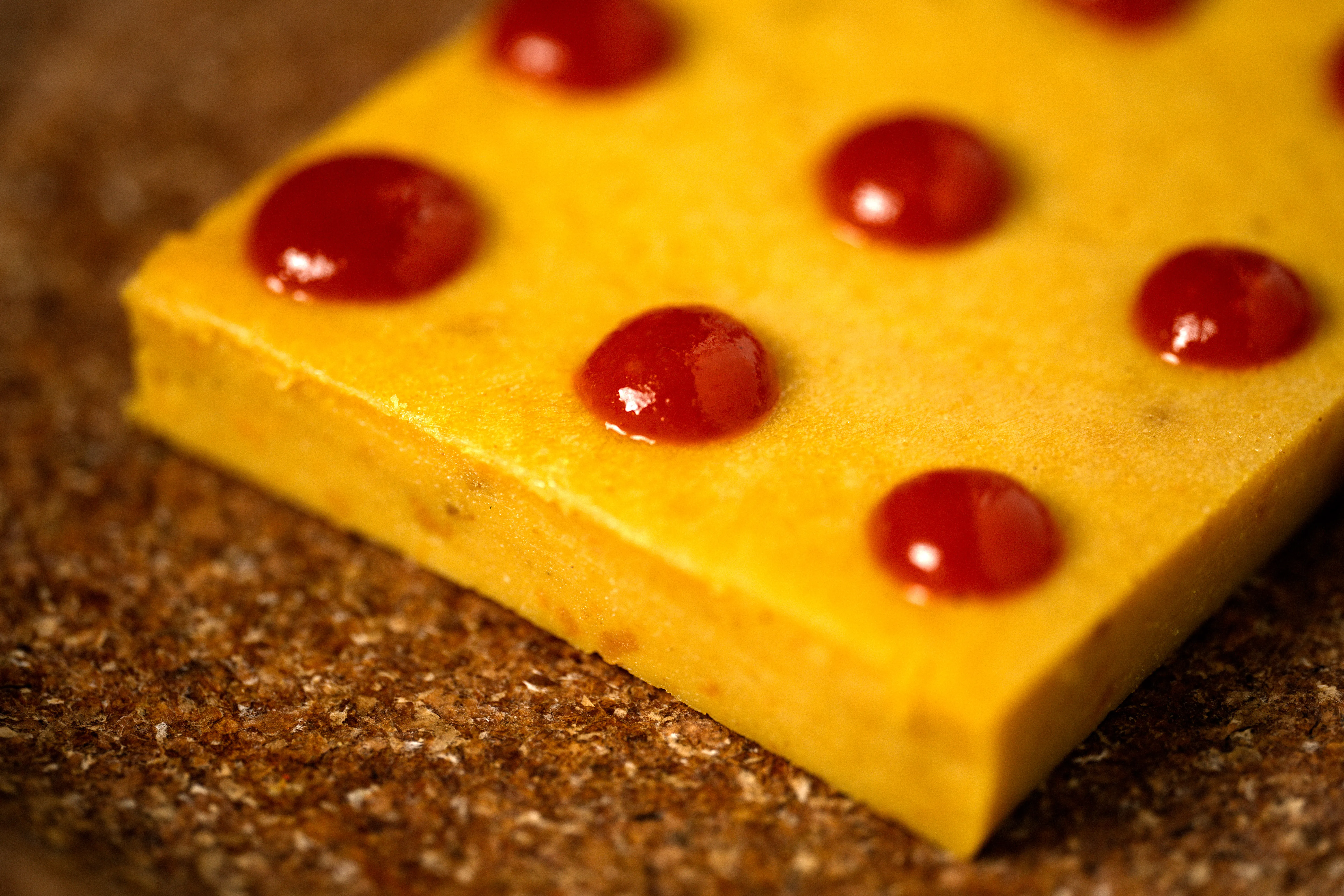 A yellow gelatin dessert with red fruit sauce dots, shot graphically against black