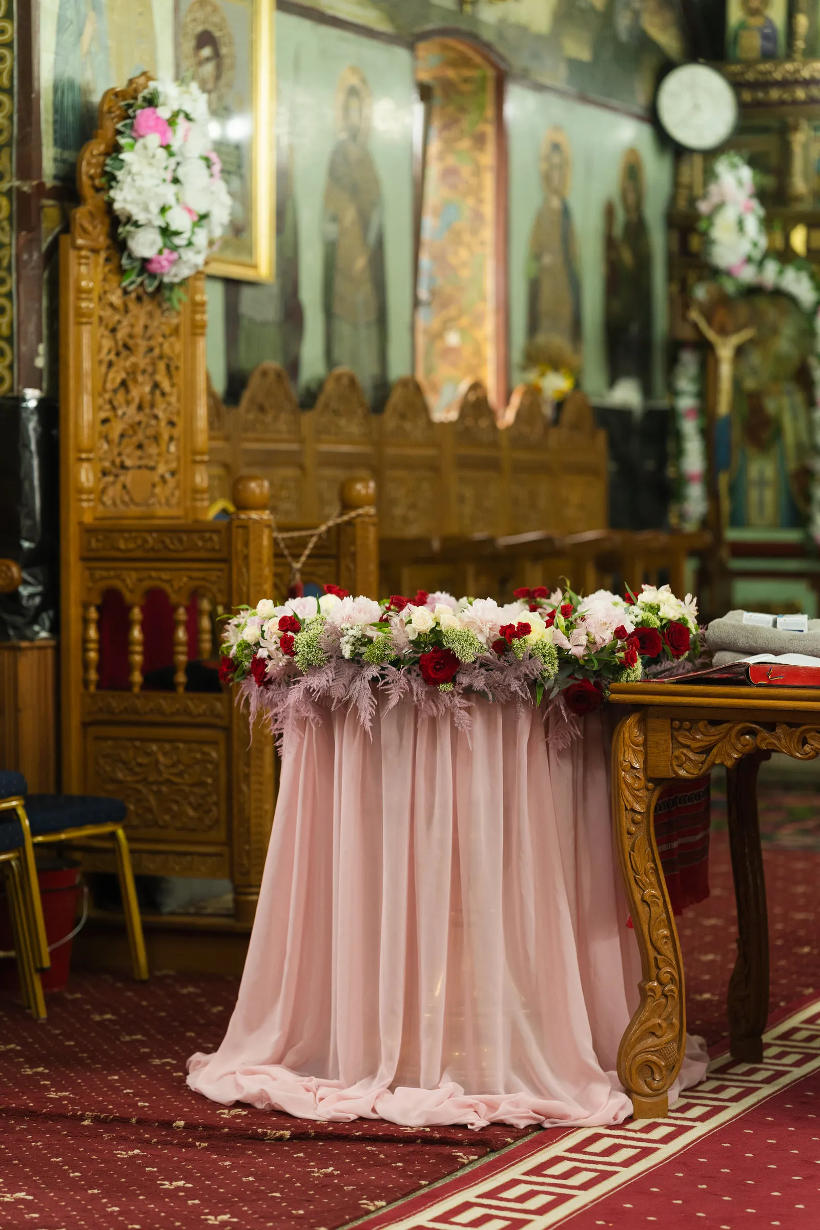The church altar dressed for the baptism, a table draped in blush pink with a garland of roses before the gilded iconostasis