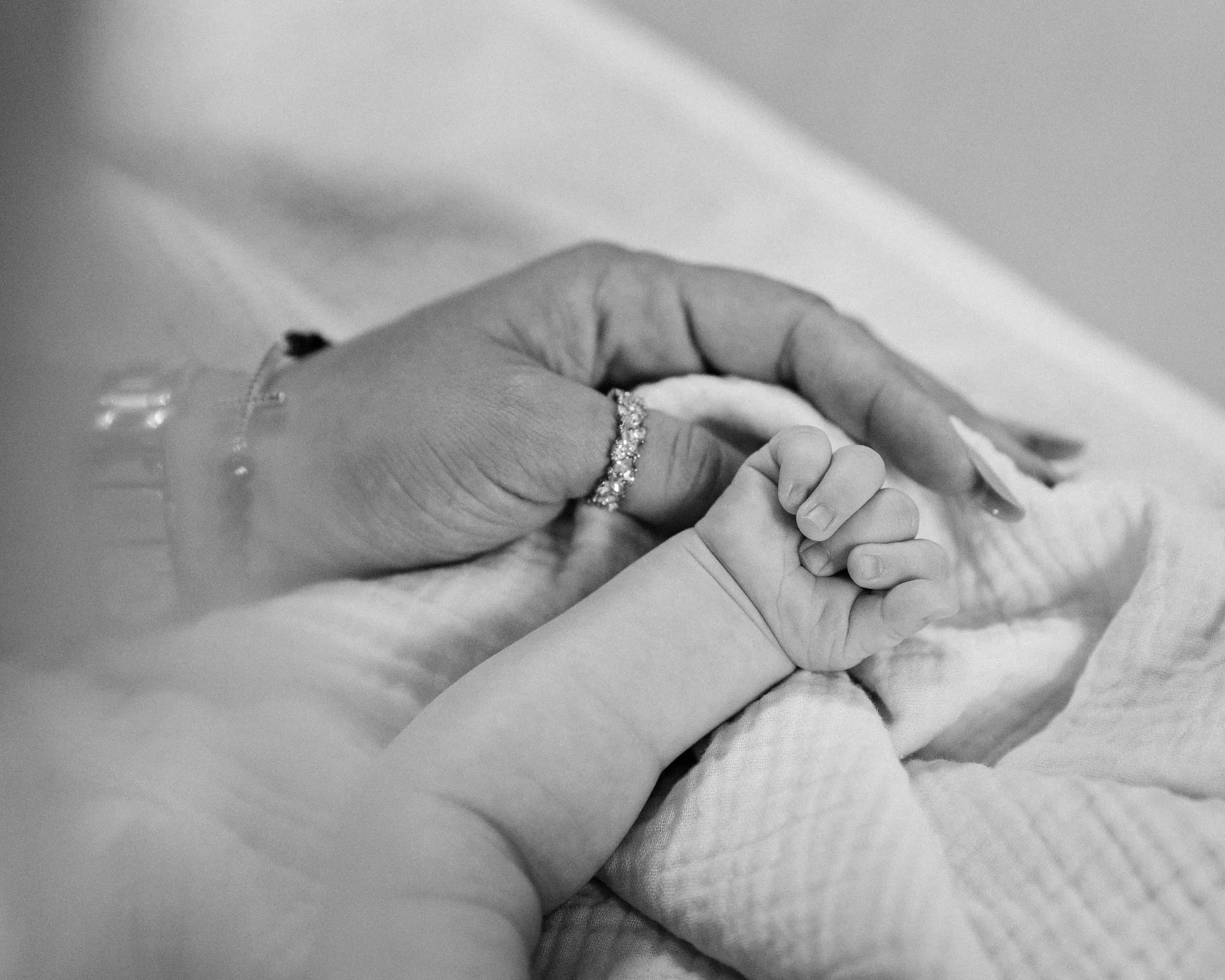Black and white detail of the baby's small fist resting against her mother's hand