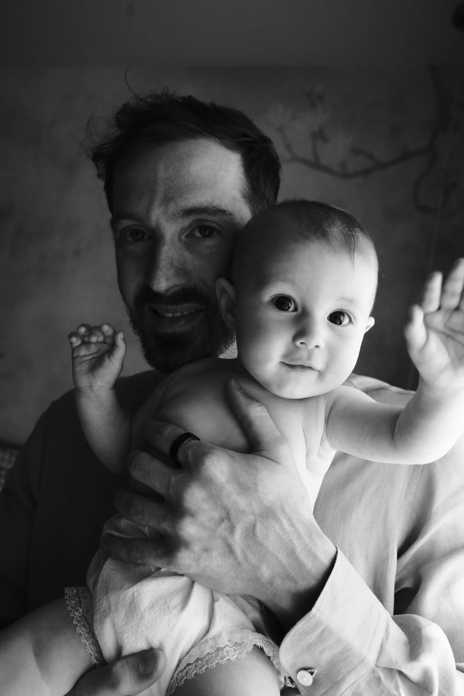 Black and white portrait of a father holding the baby, who reaches out toward the camera