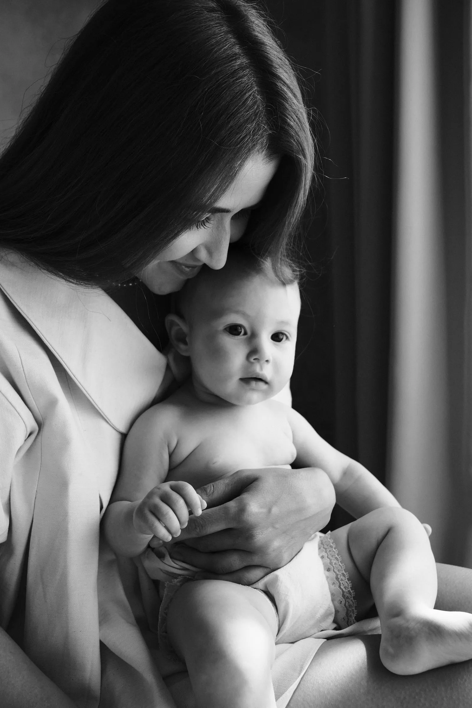 Black and white portrait of a mother resting her cheek on her baby's head as she holds her close