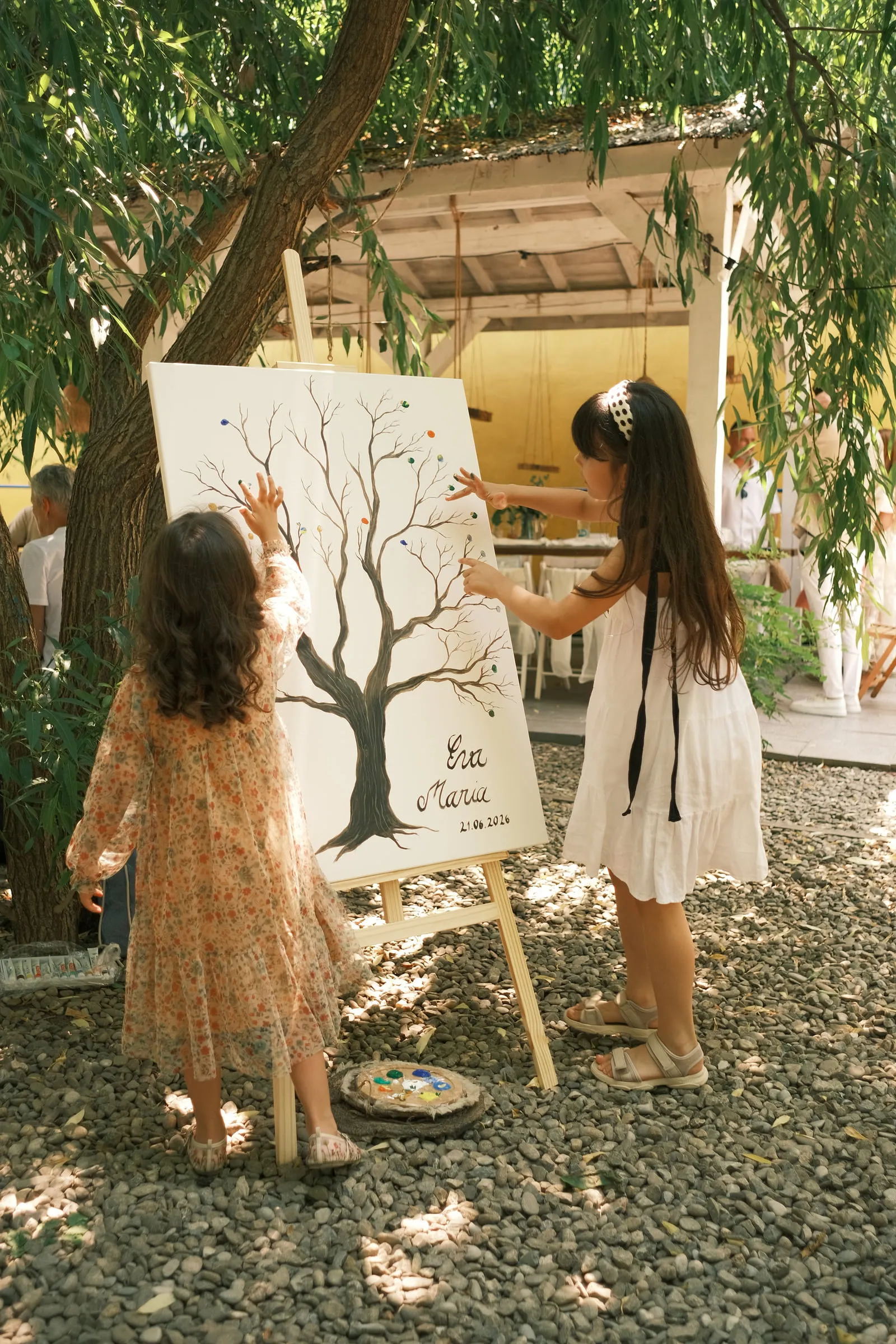 Two girls in the garden add fingerprints to a painted family tree on an easel