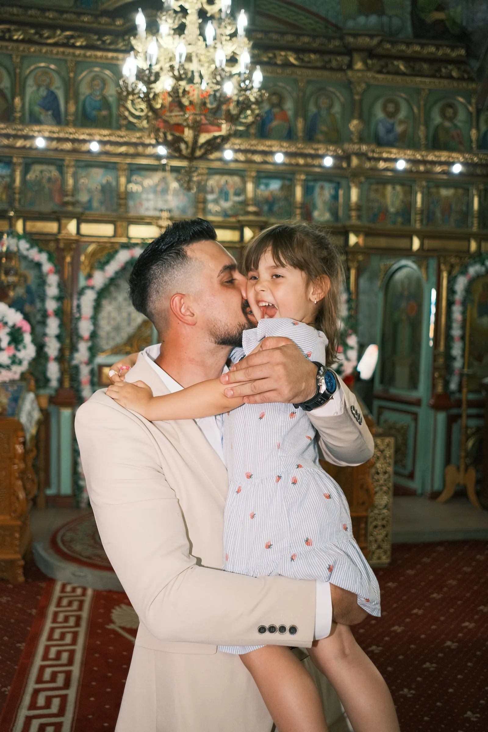 A father lifts his laughing older daughter and kisses her cheek inside the church