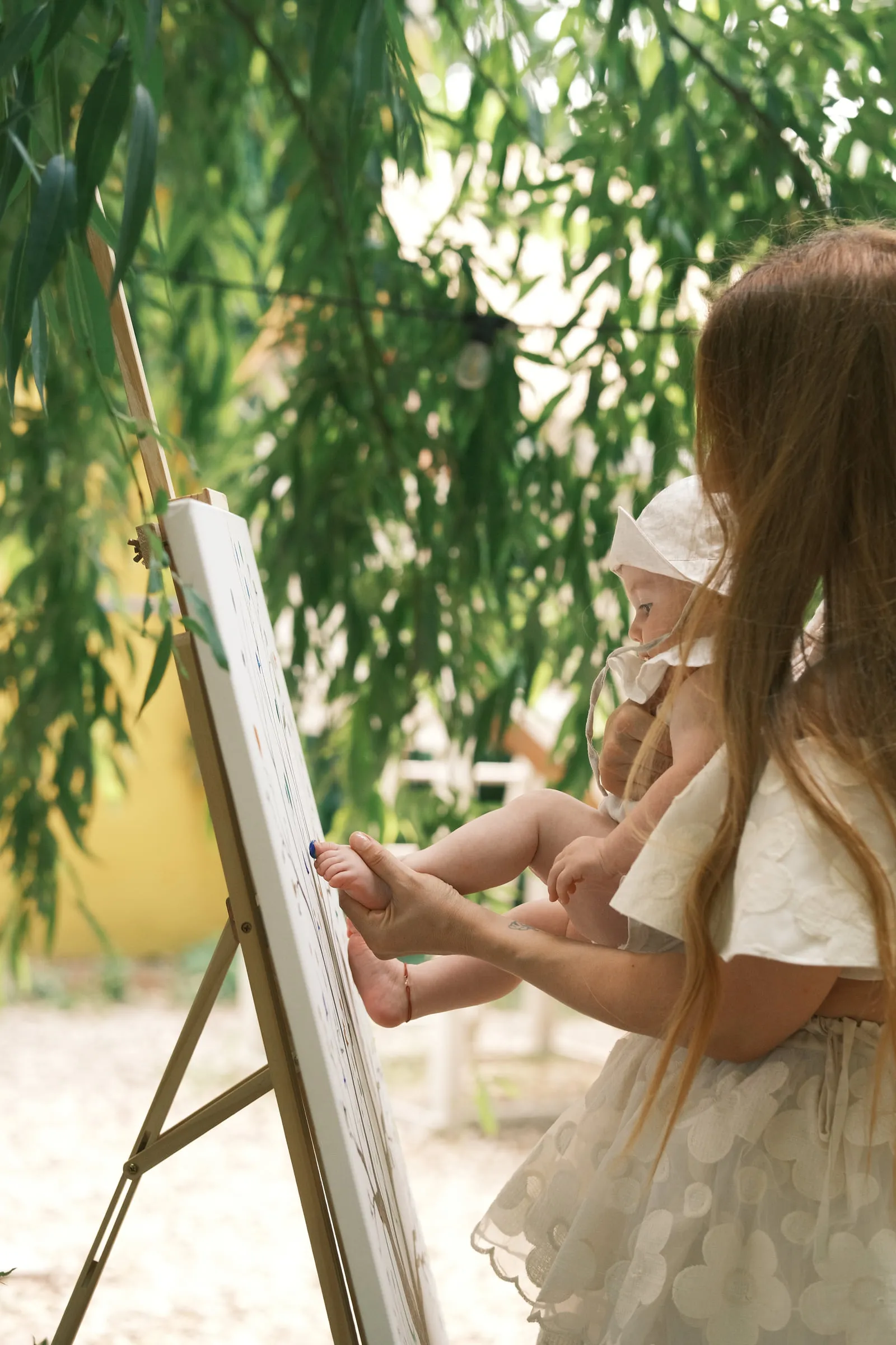 The baby's foot is pressed onto the fingerprint tree canvas, under the willow branches