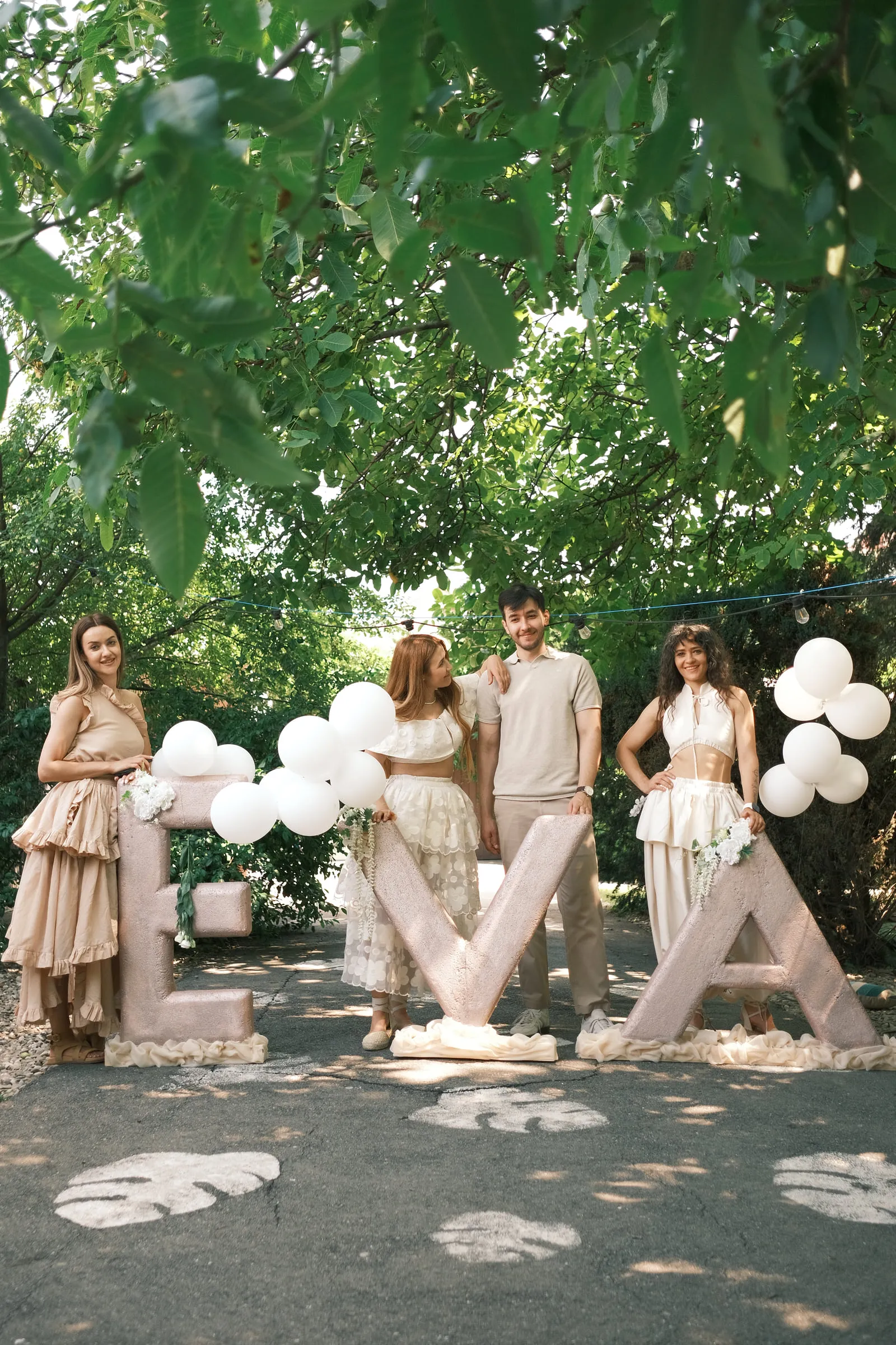 Guests stand among the large EVA letters and white balloons beneath the trees