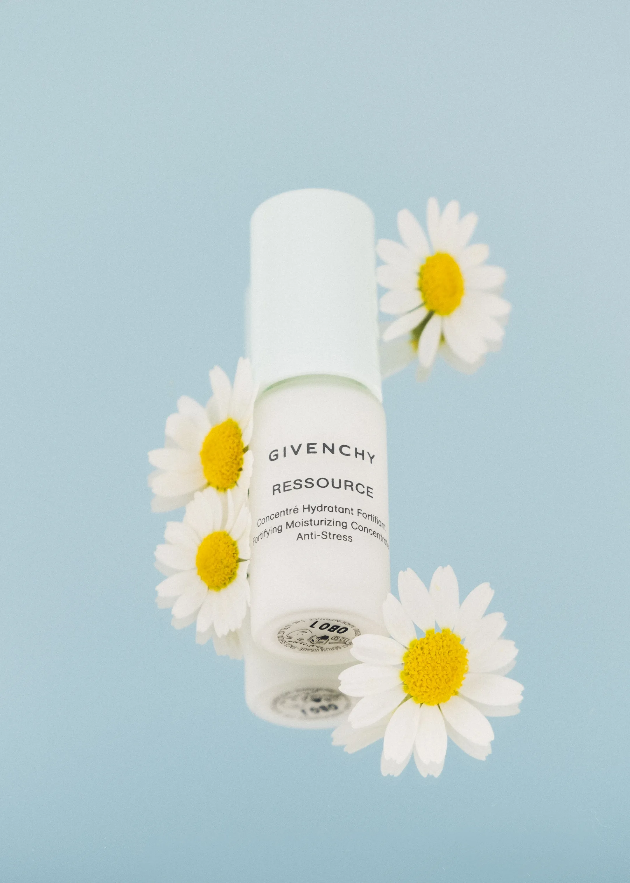 A Givenchy skincare bottle surrounded by daisies against a pale blue background