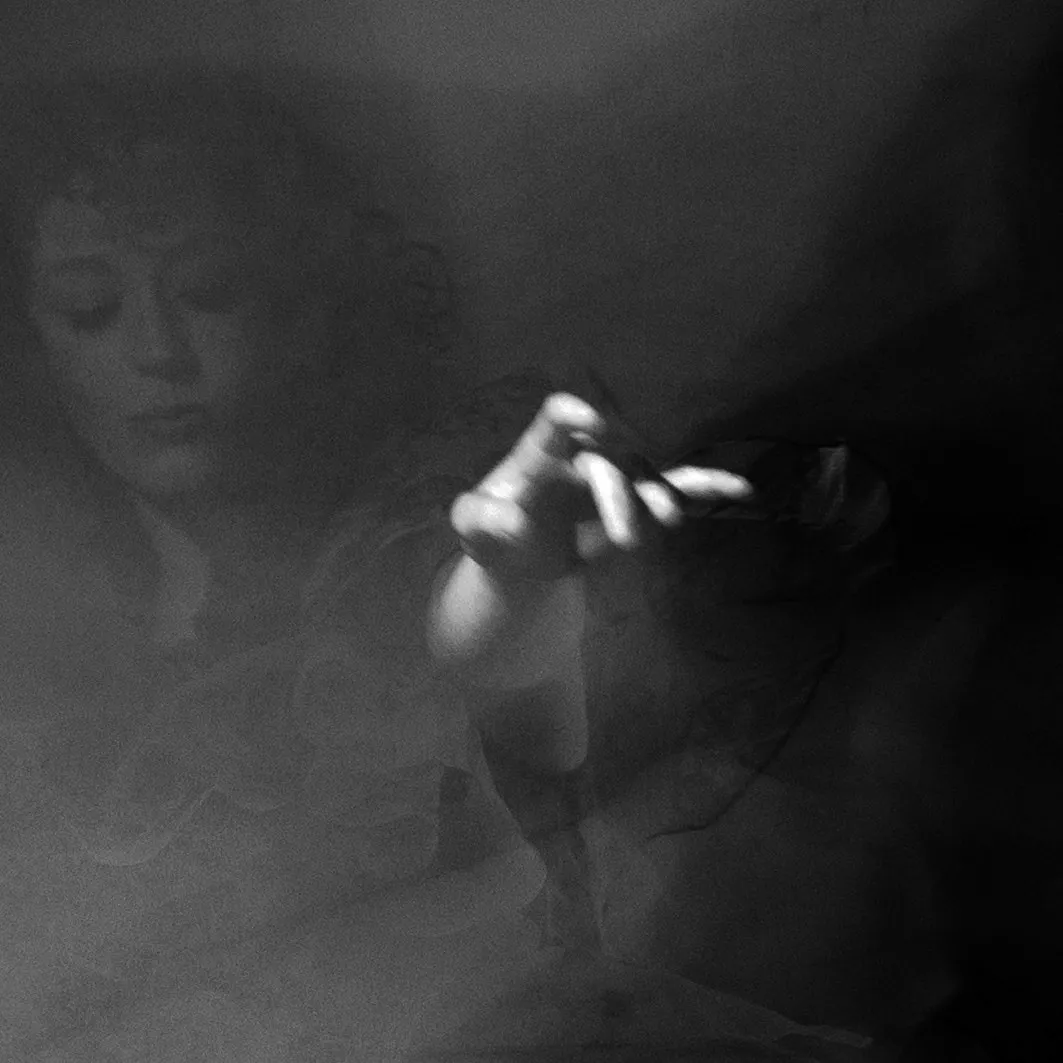 A hand reaching, softly out of focus, a face dissolving behind it