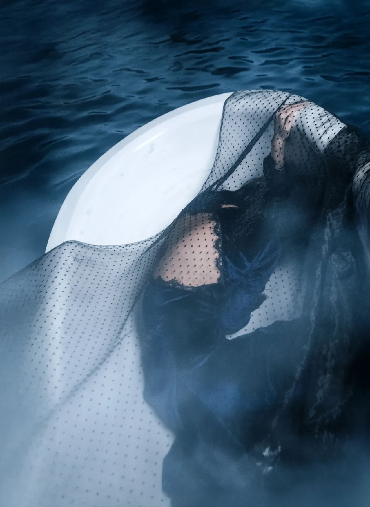 A figure submerged underwater beneath sheer draped fabric, blue tones